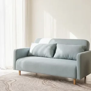 Canapé vert d'eau aux coussins bleu pâle dans un salon lumineux aux voilages blancs