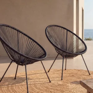 Deux fauteuils fil Acapulco noirs sur une terrasse ensoleillée avec vue sur la mer et tapis en jute