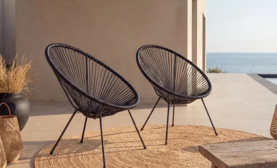 Deux fauteuils fil Acapulco noirs sur une terrasse ensoleillée avec vue sur la mer et tapis en jute