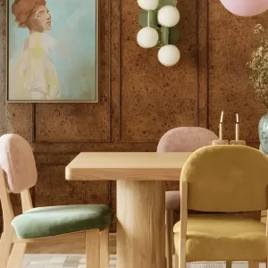 Salle à manger avec murs habillés de panneaux de liège, table en bois clair et chaises colorées en velours