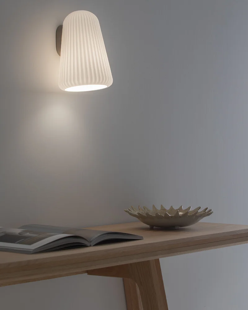 Applique murale zen en opaline blanche striée éclairant un bureau en bois clair sur mur gris
