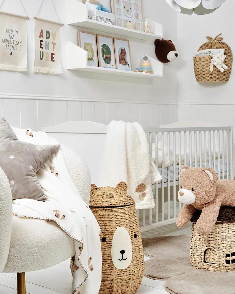 Chambre de bébé blanche avec panier ours, peluche ourson, lit à barreaux blanc et étagères murales