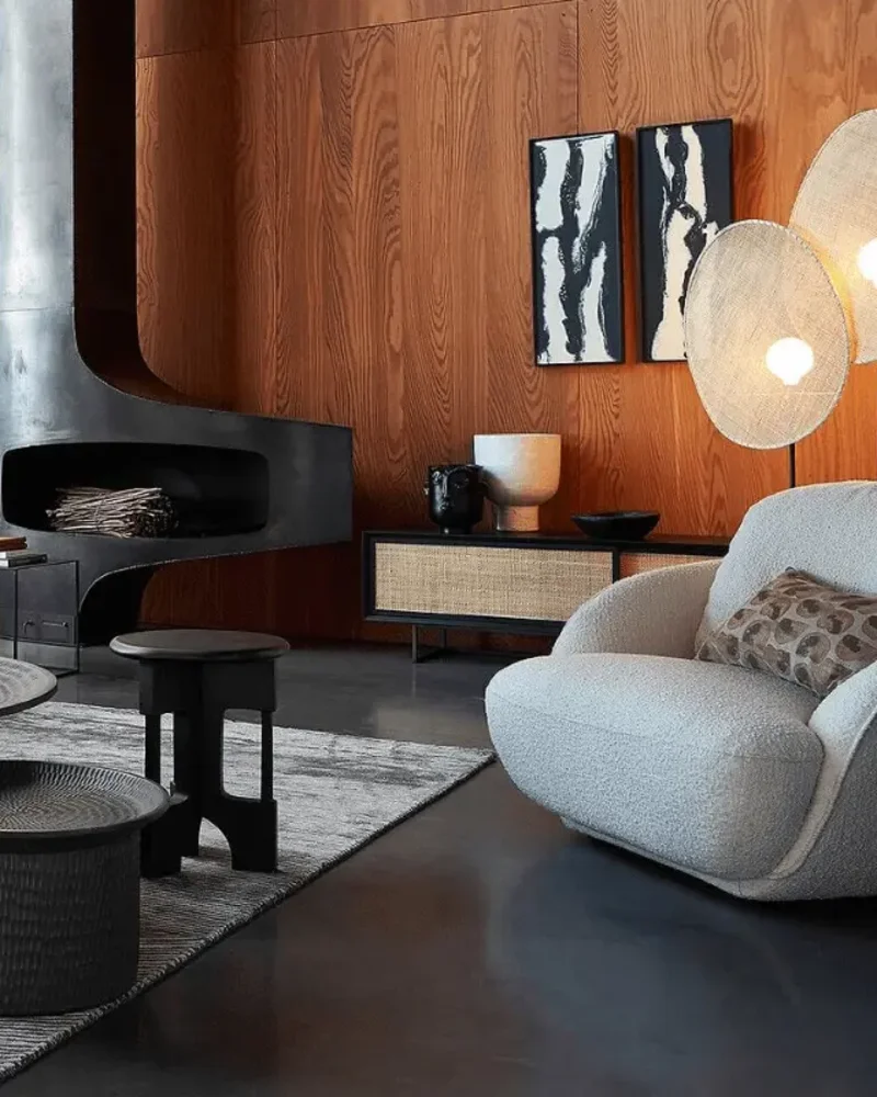 Salon chic et cosy avec cheminée suspendue en métal, fauteuil bouclette et lampadaires en fibres