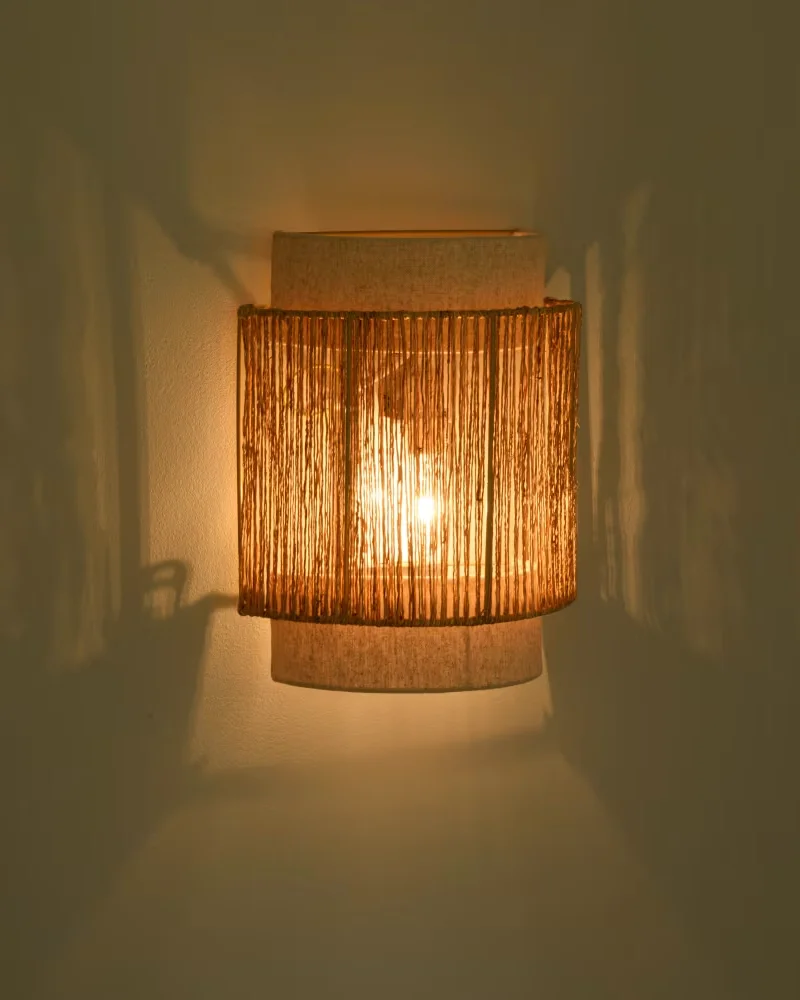 Applique murale zen en lin crème et cordes en jute diffusant une lumière chaude sur un mur sombre