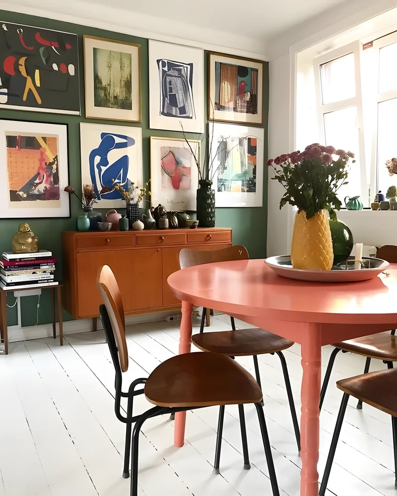 Salle à manger vintage colorée avec table rose, chaises en bois, enfilade en teck et mur de cadres