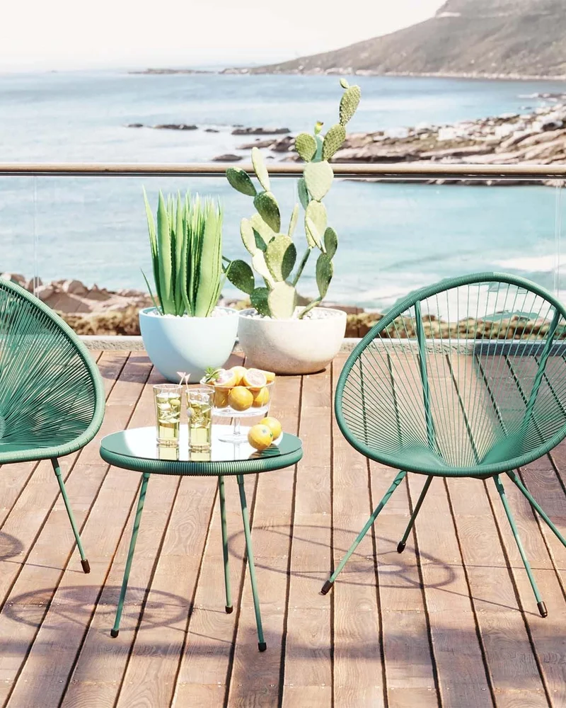 Deux fauteuils Acapulco verts et une table assortie sur une terrasse en bois face à la mer