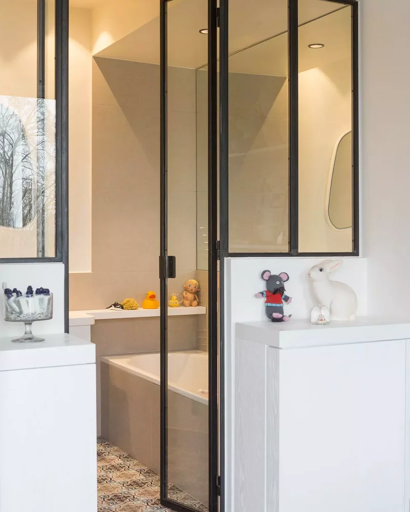 Salle de bain séparée par une verrière noire avec porte vitrée et baignoire encastrée