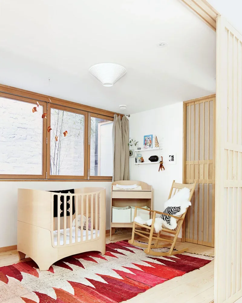 Chambre de bébé en bois clair avec lit évolutif, fauteuil en bois et tapis berbère rouge et blanc