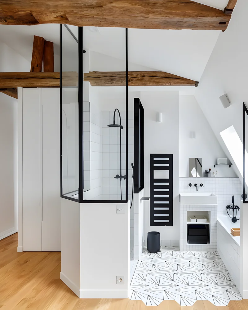 Salle de bain sous pente avec verrière noire autour de la douche, sèche-serviettes noir et parquet