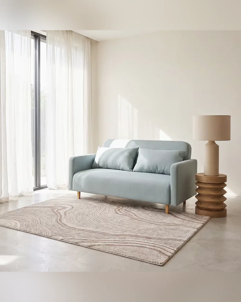 Petit canapé clic-clac vert d'eau avec coussins bleu pâle à côté d'une lampe en céramique