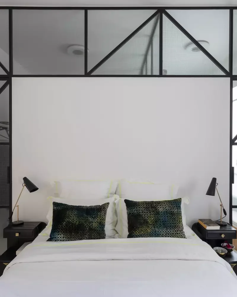 Chambre chic blanche avec verrière en métal noir encadrant la tête de lit