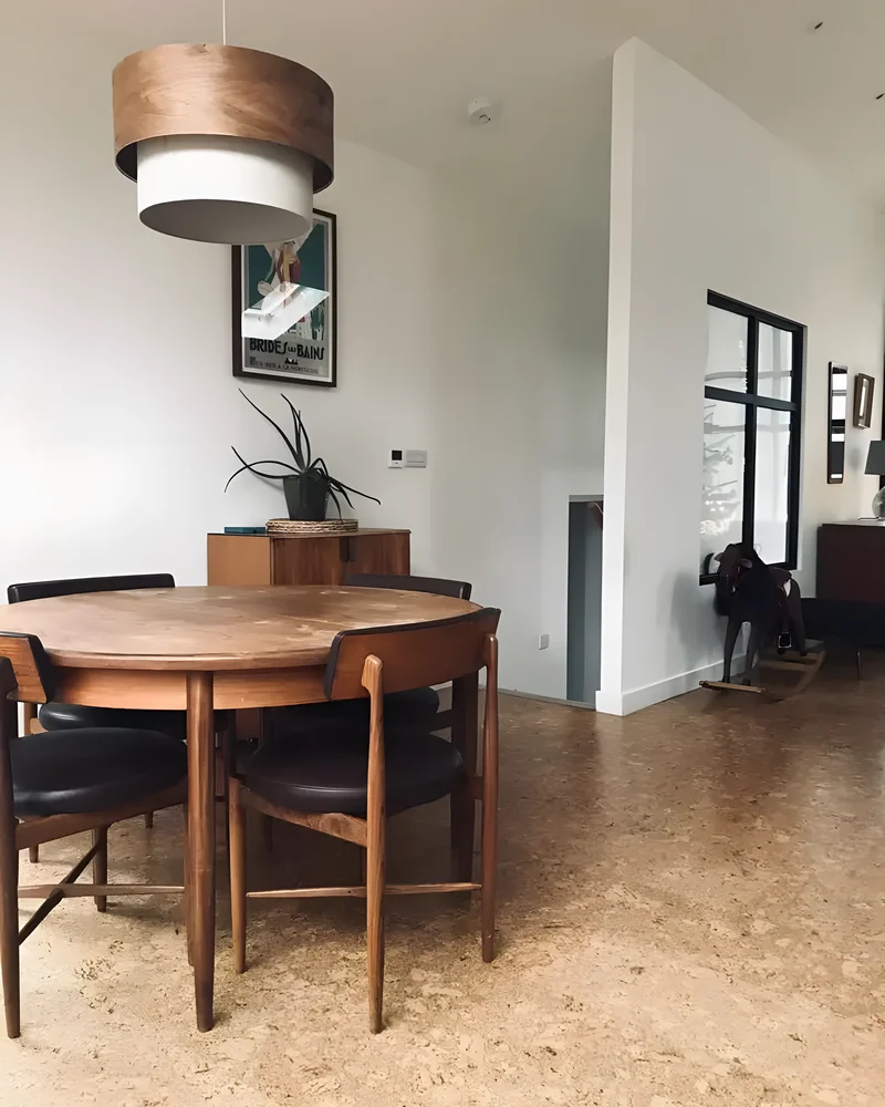 Salle à manger vintage avec sol en liège, table ronde en teck et chaises en cuir noir