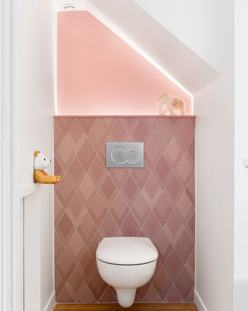 Toilettes sous pente avec carrelage rose en losange, peinture rose sur la pente et sol en bois