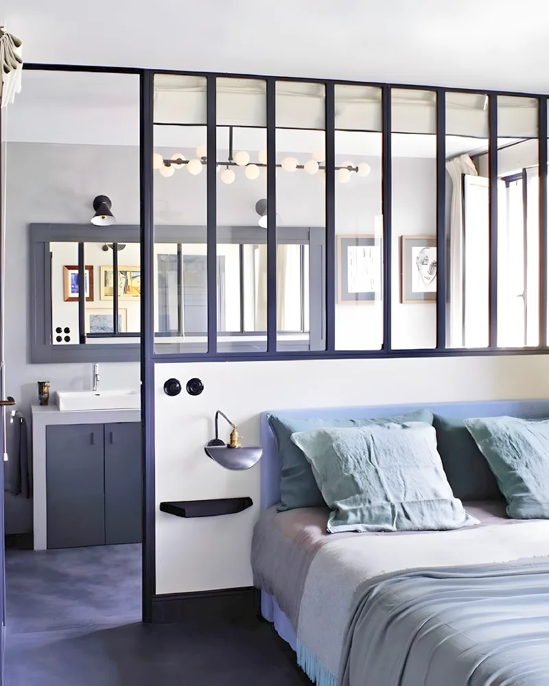 Chambre séparée de la salle de bain par une verrière noire au-dessus de la tête de lit
