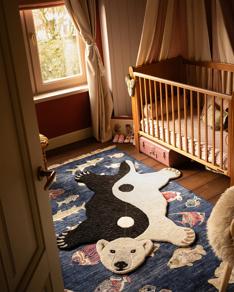 Chambre de bébé avec tapis en forme d'ours noir et blanc, lit à barreaux en bois et rideaux