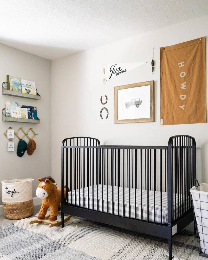 Chambre de bébé épurée avec lit à barreaux noir, étagères murales, cadre et tapis rayé