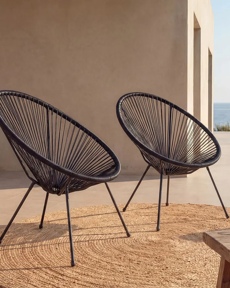 Deux fauteuils de jardin en fils de résine tressés noirs style Acapulco sur une terrasse face à la mer